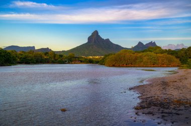 Mauritius, Tamarin Sahili 'nden Rempart Dağı' nın manzarası. Önünde sakin sular, yemyeşil alanlar ve gün batımında berrak bir gökyüzü var..