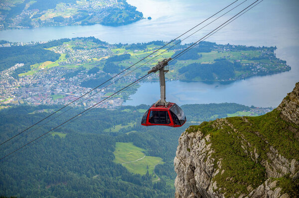 Red cable car travels toward the rocky summit of Mount Pilatus with Lake Lucerne and surrounding landscape in view.