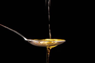 Zeytinyağı bir kaşıktan bir kaseye dökülür. fotoğraf siyah arkaplanda izole edildi