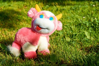 Pembe peluş bir inek yeşil bir çayırda otluyor. Sıcak, güneşli bir gün.