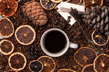 Kahve çekirdekleri üzerinde beyaz bir fincan kahve, açık mavi ahşap bir masanın üzerinde. Tahta masa. Kozalaklar masaya. Beyaz lokum. Kurutulmuş narenciye. Kahverengi arkaplan.