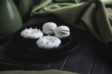 Siyah tabaklarda beyaz kremalar var. Pastel renklerde bir hayat. Koyu, ahşap bir masada yeşil bir bez..