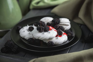 Siyah bir tabakta beyaz krema ve marşmelov, kırmızı şurupla doldurulmuş. Çilek şurubu. Tatlı böğürtlenlerle süslenir. Siyah böğürtlen ve beyaz kurabiye. Karanlık ahşap bir masada hayat.