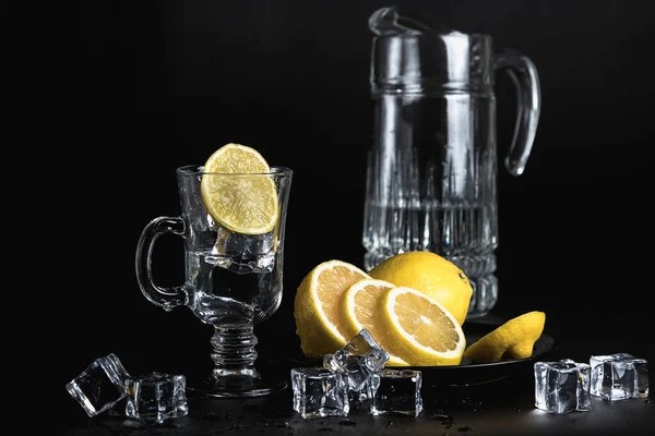 黒を背景に生活している ガラスと氷 冷たい飲料水 黒い皿の中の黄色いレモン — ストック写真