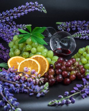 Bardakta kırmızı şarap, Üzüm ve Asma, siyah arka planda turuncu. Çiçekler lupinli. Güzel, alkollü sakin bir hayat..