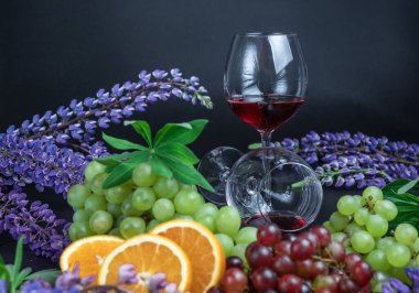 Masada bir bardak kırmızı şarap var. Siyah arka planda güzel, sakin bir hayat. Üzümlerin, portakalların ve lupin çiçeklerinin durgun yaşamı.