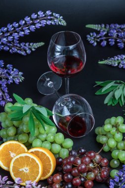 Masada bir bardak kırmızı şarap var. Siyah arka planda güzel, sakin bir hayat. Üzümlerin, portakalların ve lupin çiçeklerinin durgun yaşamı.