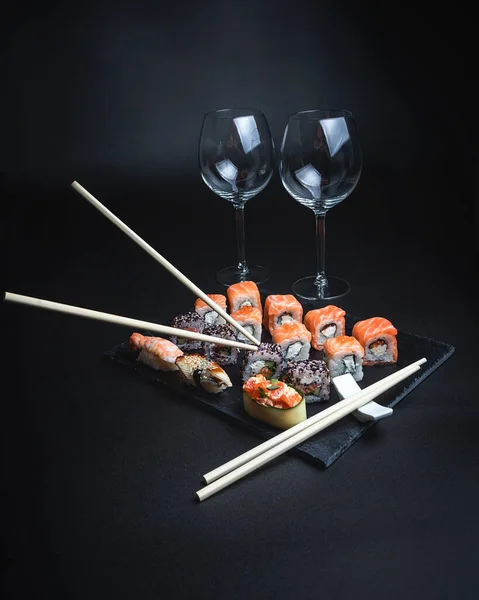 Sushi with red wine on a dark restaurant background. Chopsticks. A glass of wine. Soy sauce. Rolls and sushi. Japanese cuisine.
