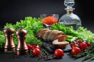 Soğuk Tütsülenmiş balık dilimleri. Kapat. Balık ve sebzelerle dolu bir hayat. Cam kasede kırmızı havyar. Biberlik ve tuzluk. Koyu bir arka planda yemek.