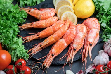 Büyük taze karidesler. Sebzeli ve otlu deniz ürünleri. Domates ve salata. Karanlık bir arka planda hayat.