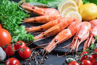 Büyük taze karidesler. Sebzeli ve otlu deniz ürünleri. Domates ve salata. Karanlık bir arka planda hayat.