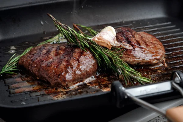 Fresh beef meat cooked on a grill pan. Meat is fried in butter. Steak with rosemary. Stripes on the meat. Fluted frying pan.