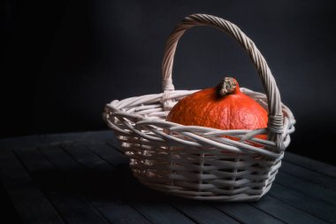 Balkabağı beyaz bir sepetin içinde, siyah bir arka planda..