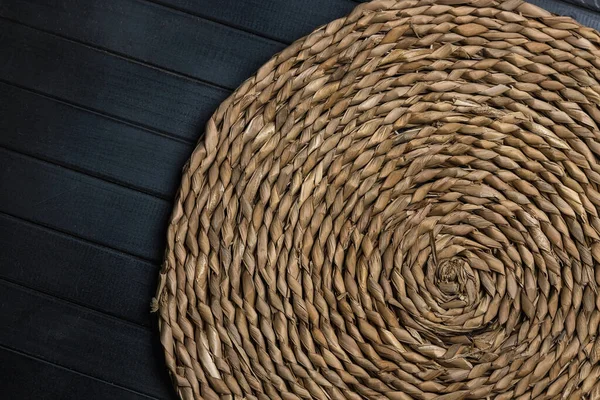 Doğal hasır masa. Mat yuvarlak hasır, merkez spiral, karanlık tahtalardan yapılmış bir masanın üzerinde.