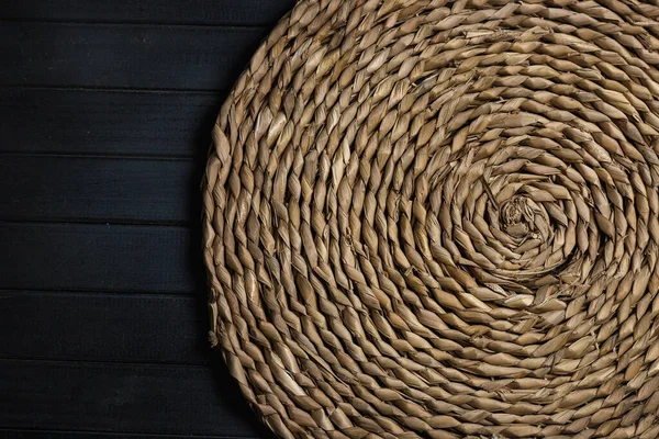 Doğal hasır masa. Mat yuvarlak hasır, merkez spiral, karanlık tahtalardan yapılmış bir masanın üzerinde.