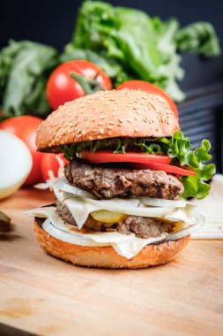 Sebzelerin arka planına karşı tahtadan yapılmış sulu bir hamburger..