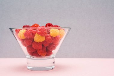 Kopya alanı ile gri pembe arka plan üzerinde sarı ve kırmızı ahududu meyveleri. Dut tatlısı. Sağlıklı bir diyet için arka plan. Sağlıklı beslenme konsepti.