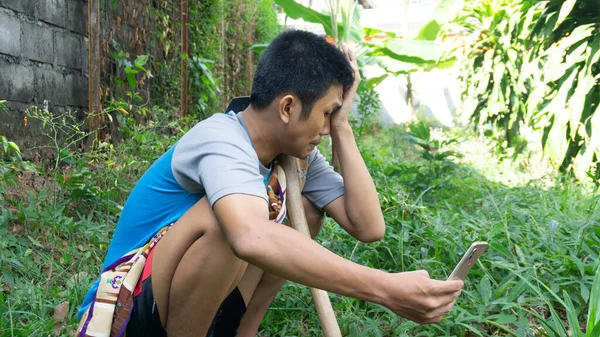 Aziatische Man Tuinieren Verdrietig Terwijl Kijken Naar Zijn Mobiele Telefoon — Stockfoto