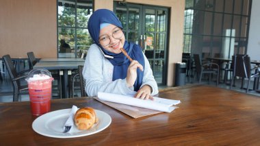 Asyalı iş kızı not alıyor ve telefonla konuşuyor.