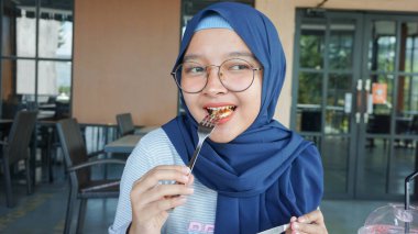 Asyalı tesettürlü kadın ekmek yiyor.