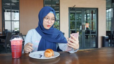 Asyalı tesettürlü kadın heyecanlandı ve bir cep telefonuna baktı.