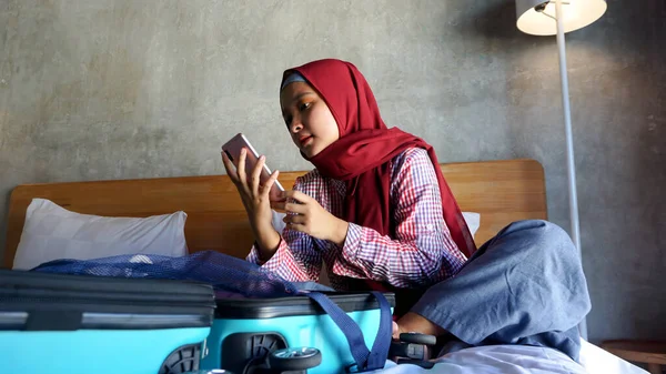 アジアのヒジャーブ女の子遊び携帯電話とオープンスーツケース — ストック写真