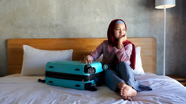 Asian hijab girl thinks in the bedroom with a suitcase