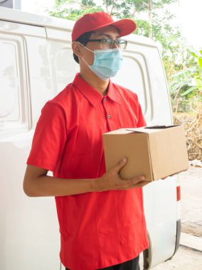 Asyalı genç adam paketlerle kırmızı üniformayla teslimat yapıyor.