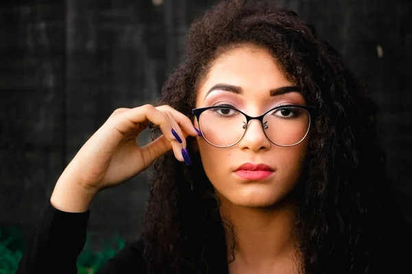 Black teen girl in glasses, photo with dark background. Girl with long curly hair. Diversity