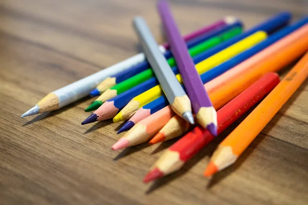 Lapis coloridos dispostos em cima de uma mesa com textura amadeirada. Cores dos lapis azul, roxo, rosa, vermelho, laranja e prata.