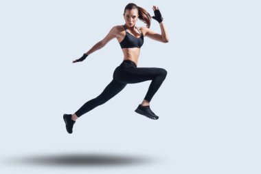 Şimdi hareket et! Gri arka plana karşı vurgulama ederken kamera bakarak spor giyim çekici genç kadının tam uzunluğu