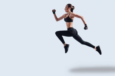 En iyi sonuçları elde etmek. Gri arka plana karşı vurgulama ederken egzersiz spor giyim çekici genç kadın tam uzunluğu