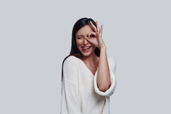 Juguetón. Atractiva joven mujer sobresaliendo de la lengua y sonriendo mientras está de pie sobre fondo gris —  Fotos de Stock