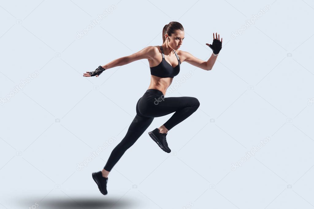 Full of energy. Full length of attractive young woman in sports clothing jumping while hovering against grey background