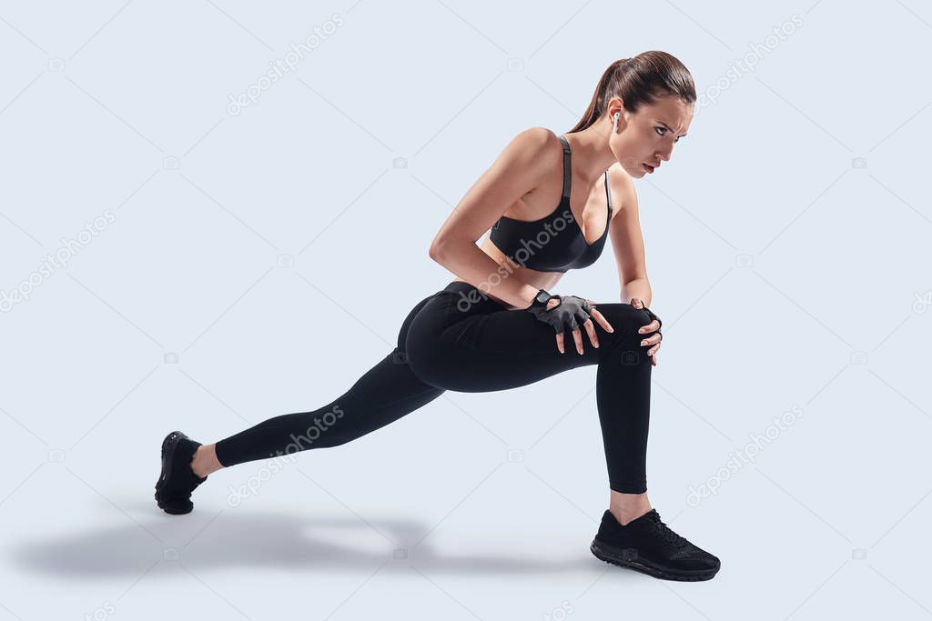 Always in shape. Attractive young woman stretching while exercising against grey background