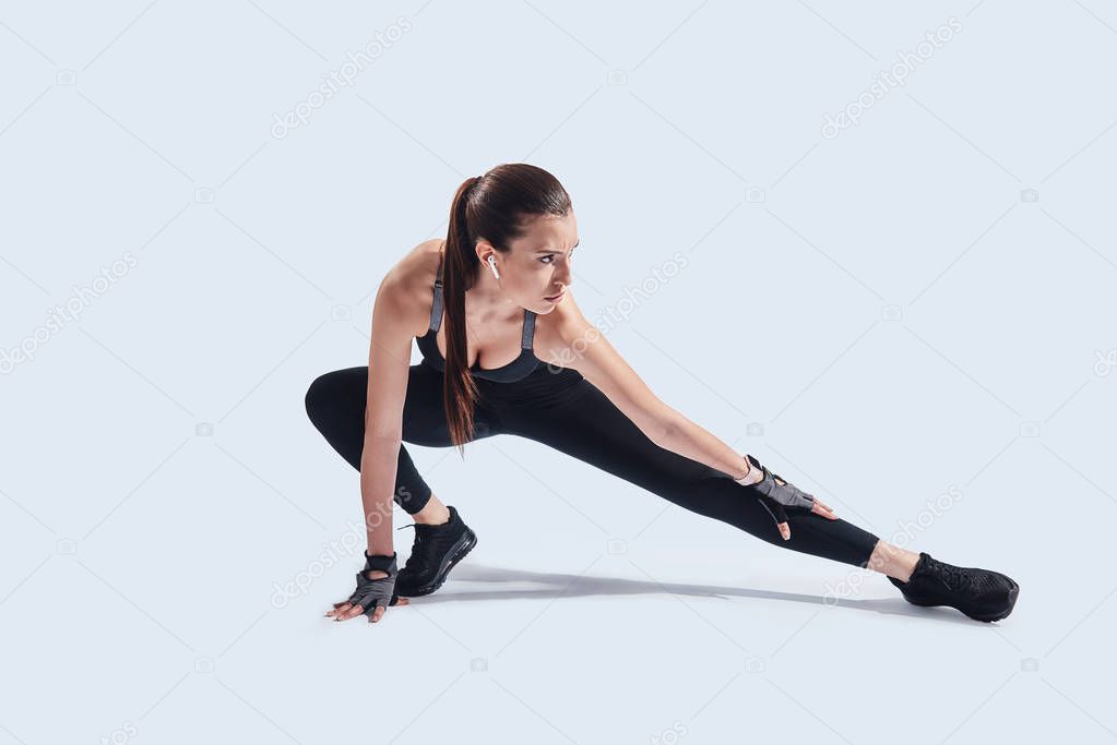 Motivated to shape her body. Attractive young woman stretching while exercising against grey background