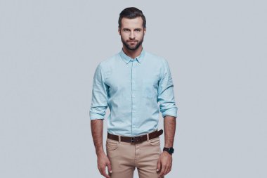 Çekici adam. Yakışıklı genç adam kamera bakıyor ve gri arka planda ayakta iken gülümsüyor