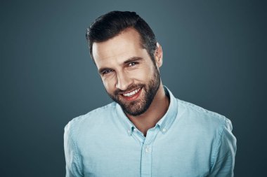 Samimi bir gülümsemesi var. Yakışıklı genç adam kamera bakıyor ve gri arka planda ayakta iken gülümsüyor