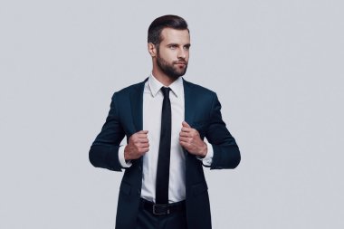 Genç ve başarılı. Gri arka planda ayakta iken ceketini ayarlayarak yakışıklı genç adam