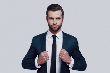 Emin müdür. Yakışıklı genç adam kamera bakıyor ve gri arka planda ayakta iken ceketi ayarlama