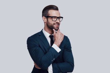 İş hakkında düşünüyorum. Yakışıklı genç adam çene üzerine el tutarak ve uzak gri arka planda ayakta bakıyor