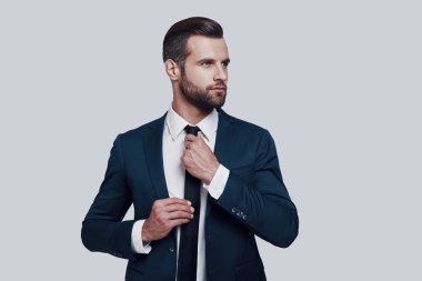 En iyi olmaya hazırlanıyor. Gri arka plana karşı ayakta iken yakışıklı genç adam kravat ayarlama