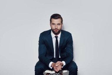 Her yönden mükemmel. Gri arka planda otururken kamera bakarak yakışıklı genç adam