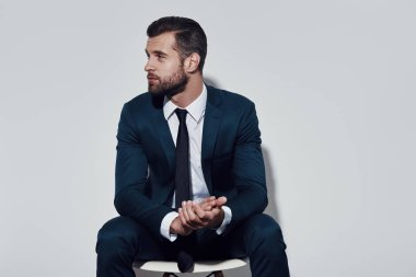 Ne yapmalı? Gri arka plana karşı otururken yakışıklı genç adam uzak bakıyor