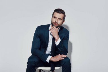 Çözüm yakındır. Yakışıklı genç adam uzağa bakıyor ve gri arka plana karşı otururken çeneye el tutarak