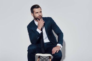 Heyecan verici bir geleceğe bakıyor. Yakışıklı genç adam uzağa bakıyor ve gri arka plana karşı otururken çeneye el tutarak