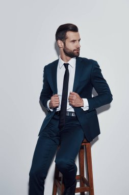 Çekici adam. Yakışıklı genç adam ceket ayarlama ve uzak gri arka planda otururken bakıyor