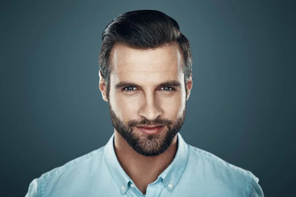 Un hombre encantador. Guapo joven sonriendo y mirando a la cámara mientras está de pie sobre un fondo gris —  Fotos de Stock