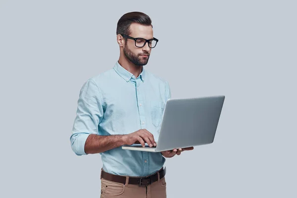현대 기술. 좋은 찾고 젊은 남자가 회색 배경에 서 있는 동안 노트북을 사용 하 여 작업 — 스톡 사진