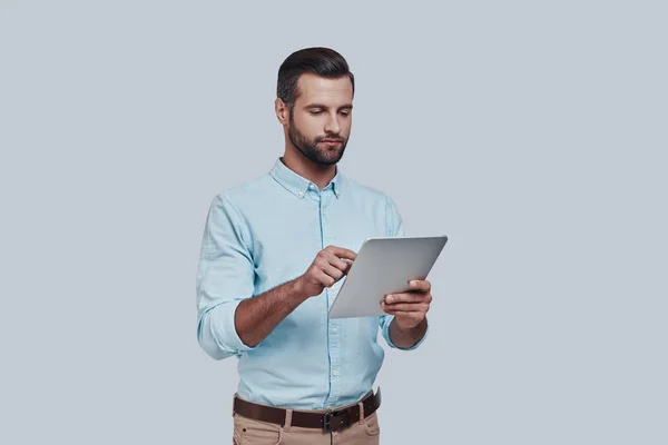 새로운 비즈니스를 계획 합니다. 회색 배경에 서 있는 동안 잘생긴 젊은 남자 디지털 태블릿을 사용 하 여 — 스톡 사진